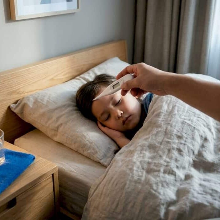 Caregiver checking child’s temperature at home